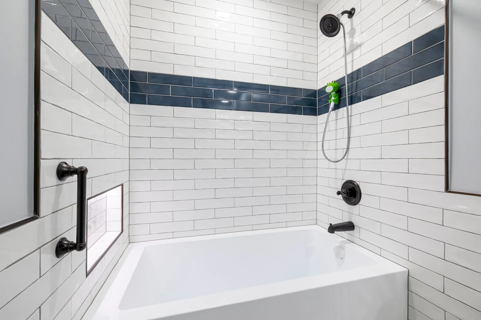 Baignoire blanche entourée de carrelage métro, avec une barre d'appui noire fixée au mur