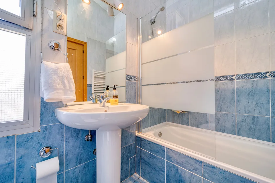 Baignoire encastrée et lavabo sur colonne dans une salle de bain au carrelage bleu
