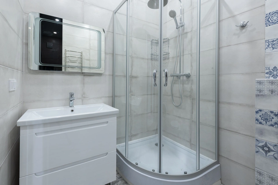 Cabine de douche arrondie posée sur un bac surélevé, à côté d'un meuble vasque blanc