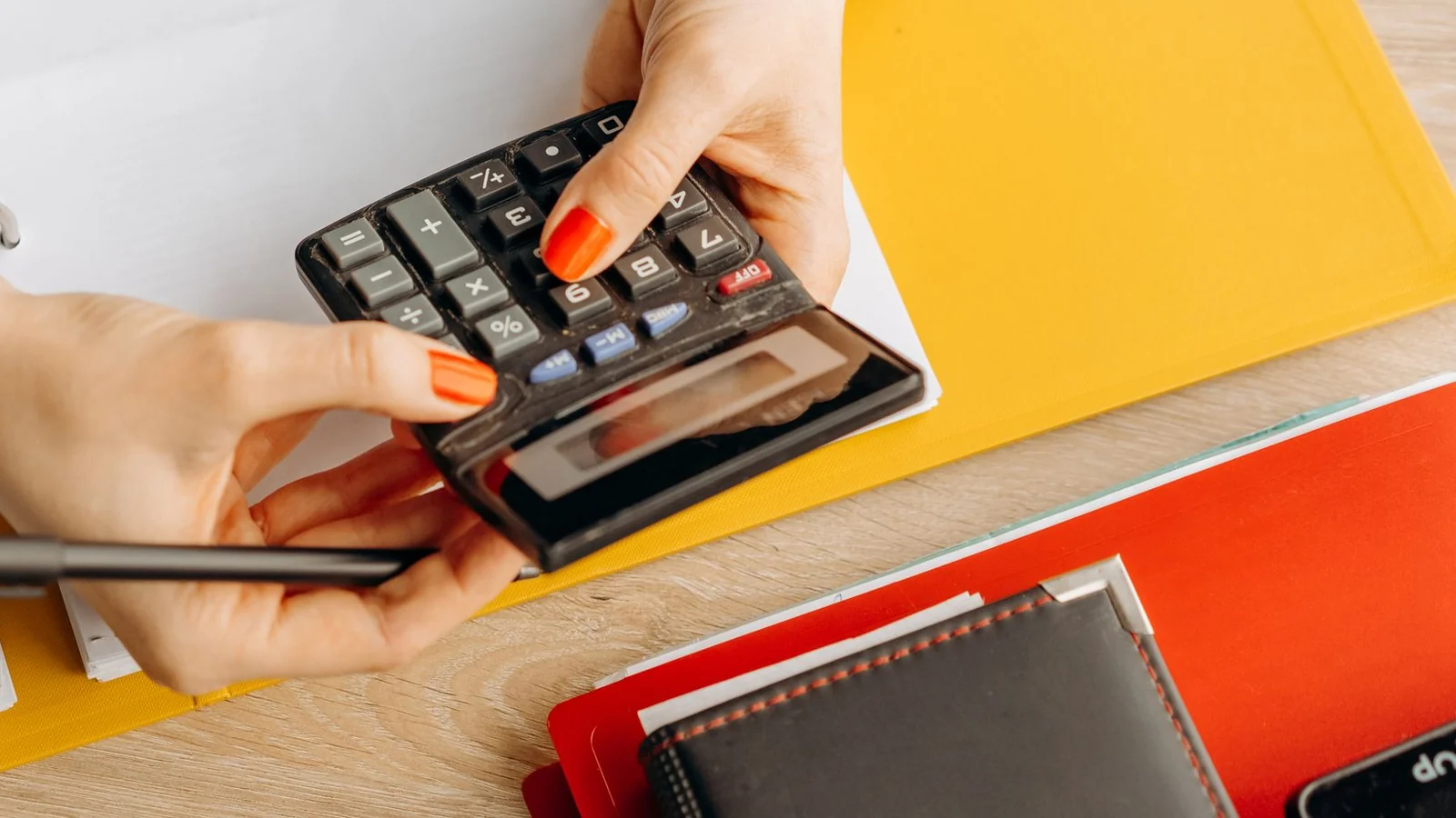 Mains tapant sur une calculatrice au-dessus d'un classeur, sur un bureau en bois