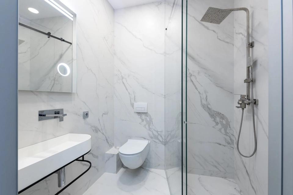 Douche vitrée de plain-pied dans une salle de bain en carrelage effet marbre blanc