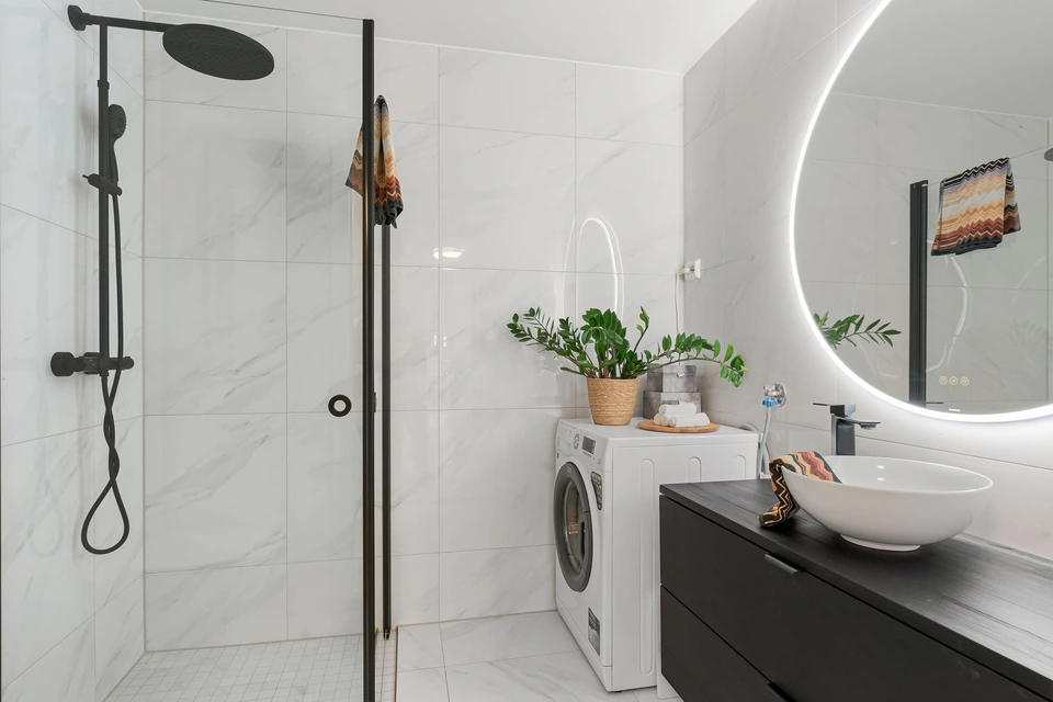 Douche à paroi vitrée et colonne de douche noire, sol plat, dans une salle de bain blanche