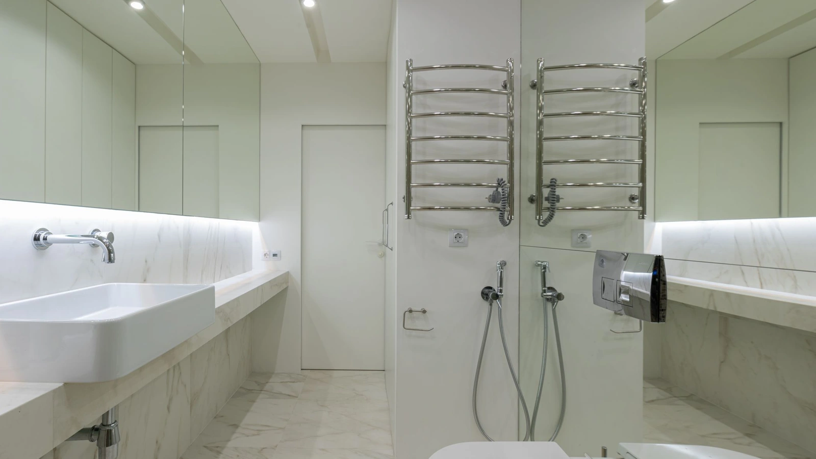 Salle de bain claire avec douche ouverte, deux sèche-serviettes chromés et plan vasque éclairé