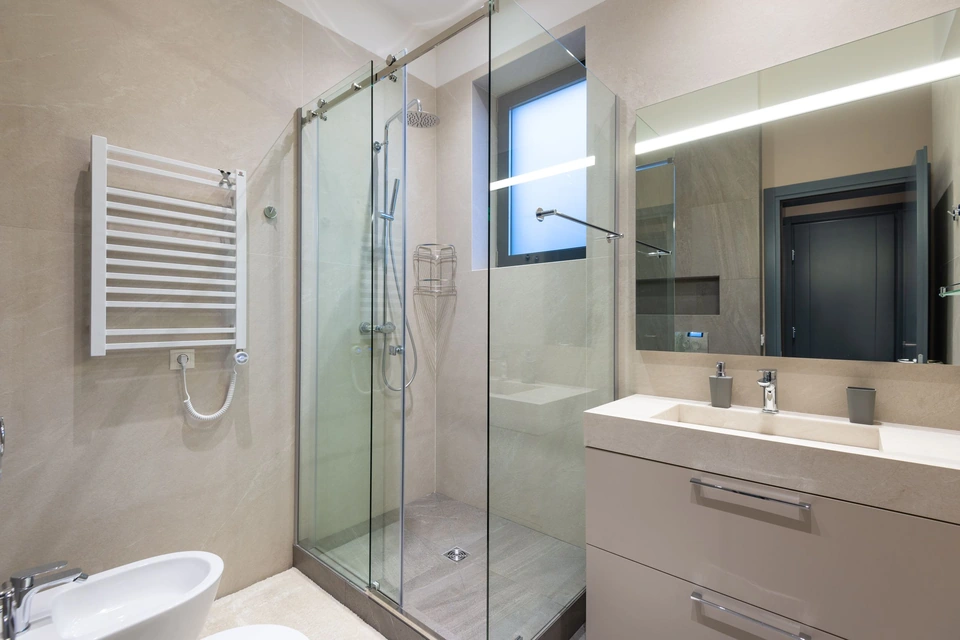 Douche fermée par des portes vitrées coulissantes, posée sur un receveur, carrelage beige